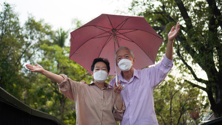 Asian senior elder couple walking in raining park share umbrella romantic love lifestyleの写真素材