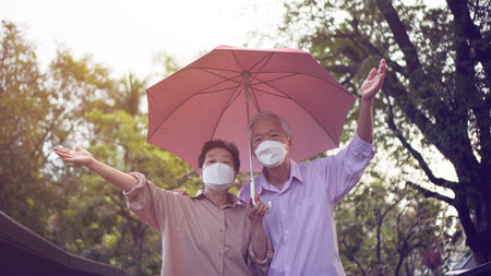 Asian senior elder couple walking in raining park share umbrella romantic love lifestyleの写真素材
