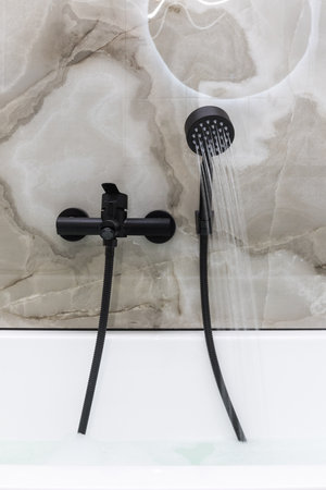 shower system with a black hose and a watering can be installed above a white bathroom with marble walls.の写真素材