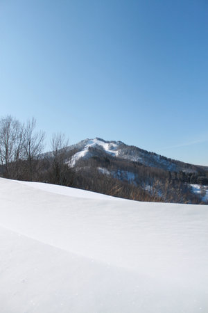Winter landscape with snow covered hill and blue sky in the background.の写真素材