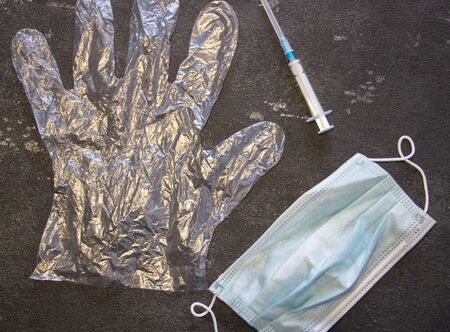 Transparent gloves, a medical mask and a medical syringe on a black background. Coronavirus and flu remedy.の写真素材