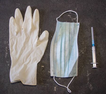 Coronavirus and Flu Control. Medical mask, syringe with a needle and rubber gloves on a black background.の写真素材