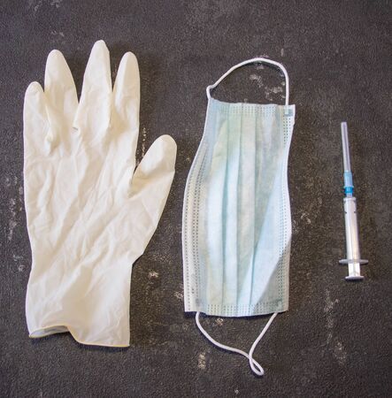 Coronavirus and Flu Control. Medical mask, syringe with a needle and rubber gloves on a black background.の写真素材