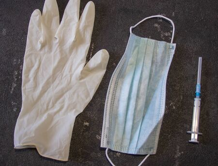 Coronavirus and Flu Control. Medical mask, syringe with a needle and rubber gloves on a black background.の写真素材