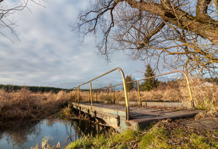 pedestrian bridge through a narrow stream in the marshland autumn cloudy weather. landscapeの写真素材