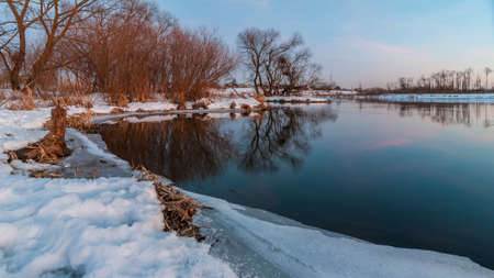 beautiful evening winter landscape. February thaw. Coast of the river with the ice edge and the vegetation under the snowの写真素材