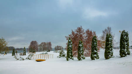 winter landscape. cloudy weather. a park zone with the pedestrian bridge through a narrow stream under snow on the coast of the lakeの写真素材