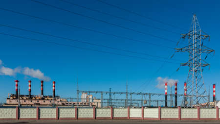Interesting industrial landscape. Factory pipes and a power line tower behind a concrete fence in the background of a clear blue skyの写真素材