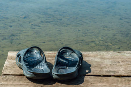 Summer rubber slippers on a wooden pier over the water. close-upの写真素材