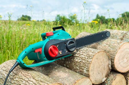 hand chain power saw on firewood against the background of a green meadow and the blue sky