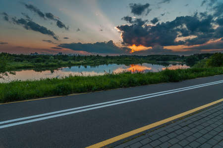 Warm quiet summer evening. Beautiful sunset over the river. City asphalt path along the river in the foregroundの写真素材