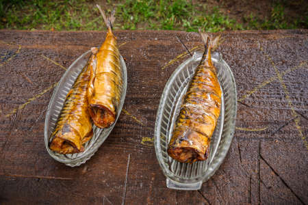 freshly prepared mackerel hot smoked in a glass plate on an old wooden background outdoors. top view