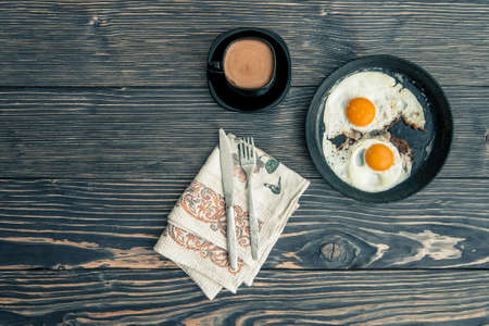 fried eggs on a cast-iron pan and a cup of coffee with milk for breakfast on an old wooden gray background. top viewの写真素材
