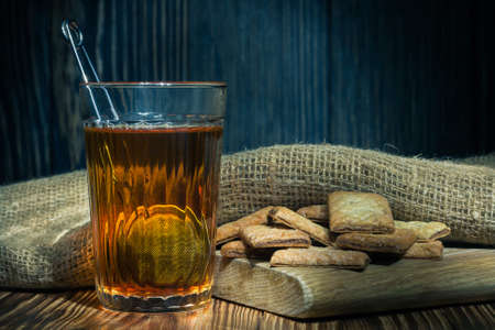 hot tea in a transparent ribbed glass with cookies on the board and sacking on a dark wooden background in a rustic styleの写真素材