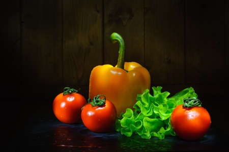 fresh vegetables with drops of water after washing on a table on a wooden background. salad set of pepper, lettuce and tomatoes. dark photoの写真素材