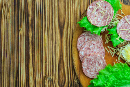 fast sandwiches of bread and butter, lettuce and salami sausages sprinkled with grated cheese for breakfast on a cutting board and on a wooden background. top viewの写真素材