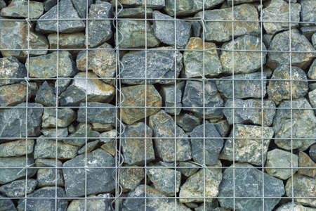 interesting creative background of gray granite medium-sized stones behind a supporting lattice of thin metal rods with square cellsの写真素材