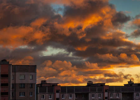 Cloudy dark sky with crimson clouds above a high-rise apartment building. side view of the upper floors and the roofの写真素材