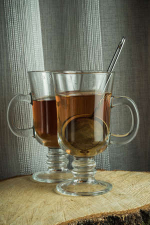 two transparent glass mugs with hot tea on a wooden cut on a textile background. minimalistic still lifeの写真素材