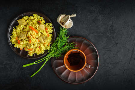 freshly prepared pilaf with tea in an earthenware bowl with a bunch of fresh dill and garlic on a black plastered concrete surface. top view. elegant dark still life for a stylish mockup with copy spaceの写真素材