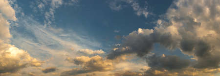 beautiful wide dramatic sky with fluffy cumulus clouds illuminated from below-side by warm...