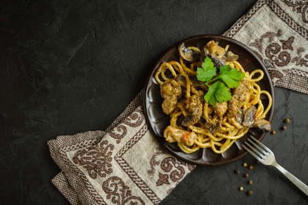 freshly prepared spaghetti with meat mushroom sauce on a plate with a kitchen napkin, metal fork and peppercorns on a black textured concrete background. top view. dark creative mockup with copy spaceの写真素材