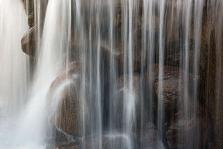 fragment of a beautiful waterfall with large old stones and vertical blurry streams and splashes. close-up side viewの写真素材