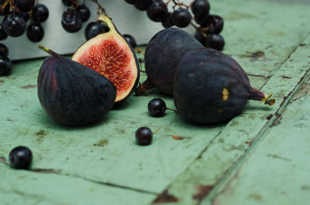 Group of figs with grapes in the background on a green vintage wooden table.の写真素材