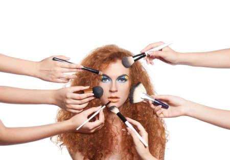 Portrait beautiful red long wavy, curly hair girl with make-up brushes near attractive face, many hands apply make up on woman face, beauty cosmetic hairstyle concept isolated over white backgroundの写真素材