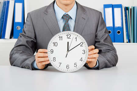 Businessman sitting at the desk at office hold clockの写真素材