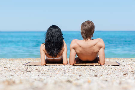 Couple on beach, rear view lying back romantic man and woman sea shore, summer ocean vacation holiday blue skyの写真素材