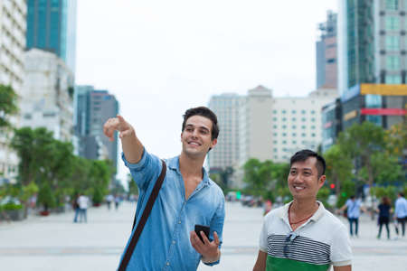 Two men tourists smile point finger sightseeing, asian mix raceの写真素材