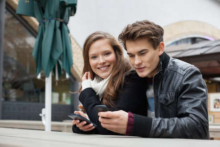 Portrait of young woman with man using cell phone at bench