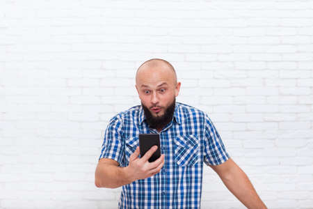 Casual Bearded Business Man Confused Surprised Holding Cell Smart Phone Office White Brick Wallの写真素材