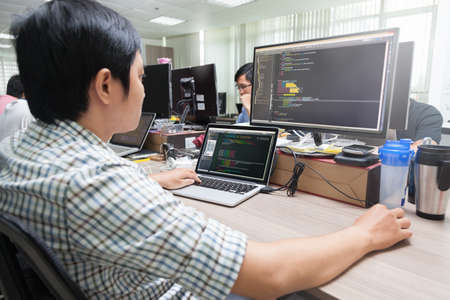 Asian Outsource Software Developer Looking Screen Sitting At Desk Working Laptop Computer Mobile...