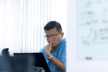 Asian Businessman Sitting Desk Working Laptop Pondering Real Office