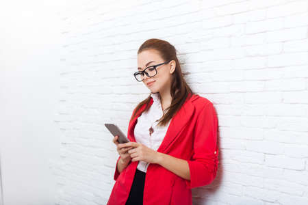 Businesswoman serious use cell smart phone wear red jacket glasses business woman over office wallの写真素材