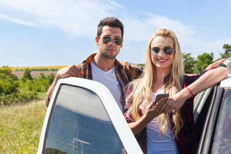 Couple near car countryside road woman hold smart phone outdoor nature blue skyの写真素材