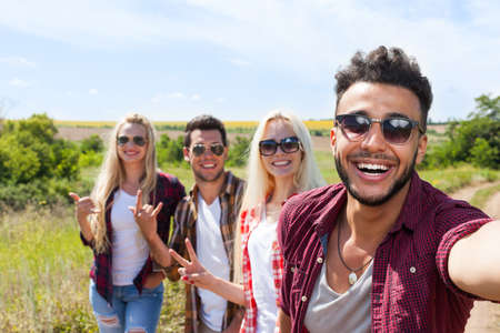 Man hold smart phone camera taking selfie photo friends face smile close up countryside young people group outdoor two couple summer sunny dayの写真素材