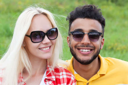 Couple face close up outdoor green grass, mix race man and woman sunglasses happy smile embrace summer dayの写真素材