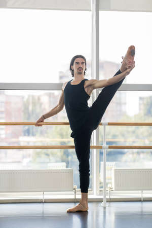 Young Male Ballet Dancer Posing Near Barre, Man Practicing Stretch In Dance Studioの写真素材