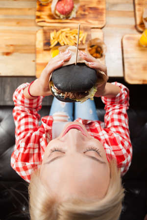 Beautiful Blonde Woman Eat Beef Burger Top Angle View, Young Girl Sitting In Fast Food Cafeの写真素材