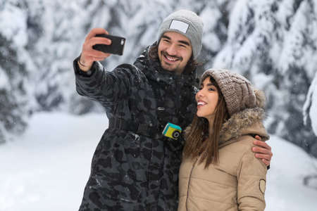 Man Hold Smart Phone Camera Taking Selfie Photo Young Romantic Couple Smile Snow Forest Outdoor...