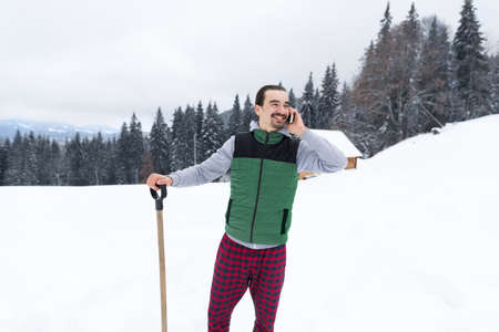 Young Man Speaking Cell Smart Phone Snowy Village Wooden Country House Winter Snow Resort Cottage Holiday Vacationの写真素材