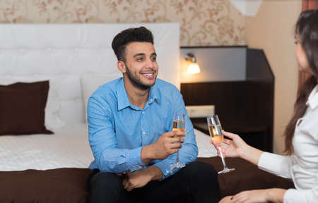 Latin Businessman Sitting At Bed In Room With Businesswoman Drink Champange Business Man And Woman Arriving To Hotelの写真素材