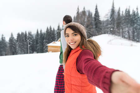 Couple Taking Selfie Photo On Smart Phone Snowy Village Wooden Country House Man Woman Winter Snow Resort Cottageの写真素材