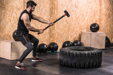 Sport Fitness Man Hitting Wheel Tire With Hammer Sledge Crossfit Training, Young Healthy Guy Gym Interiorの写真素材