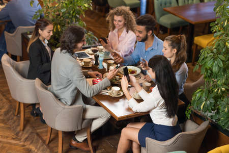 Young Business People Group Sitting Cafe Table, Friends Hold Cell Smart Phone Social Network Communicationの写真素材
