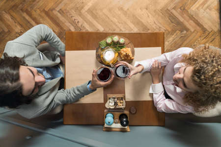 Young Couple Drink Wine Sitting Restaurant Table, Romantic Date Man And Woman Hold Glasses Clink Toasting Top Angle Viewの写真素材