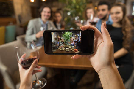Businesswoman Taking Selfie Young Business People Group Drink Wine Sitting Restaurant Table, Friends Hold Glasses Clink Toasting Smiling Mix Race Men Womenの写真素材